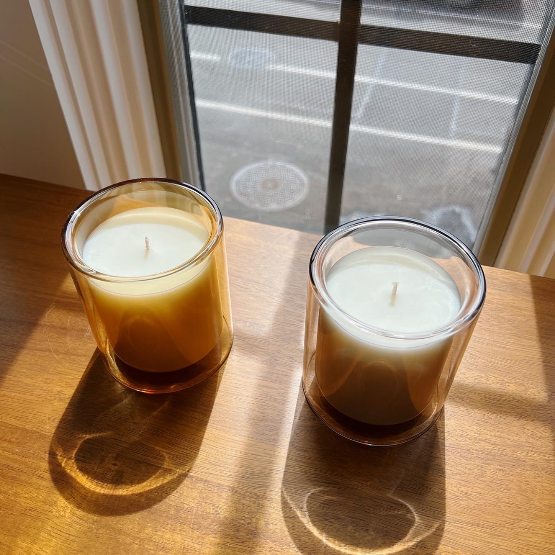 two candles on dresser shown from view from above. bedroom decor. one in marigold colored vessel (amber fragrance) and one in dove colored vessel (santal fragrance)