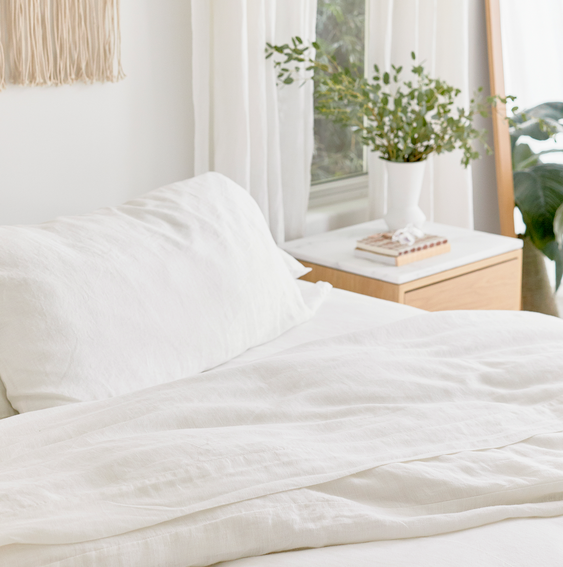 close up of corner of bed. hemp pillowcases, fitted sheet, top sheet, and duvet cover in white.