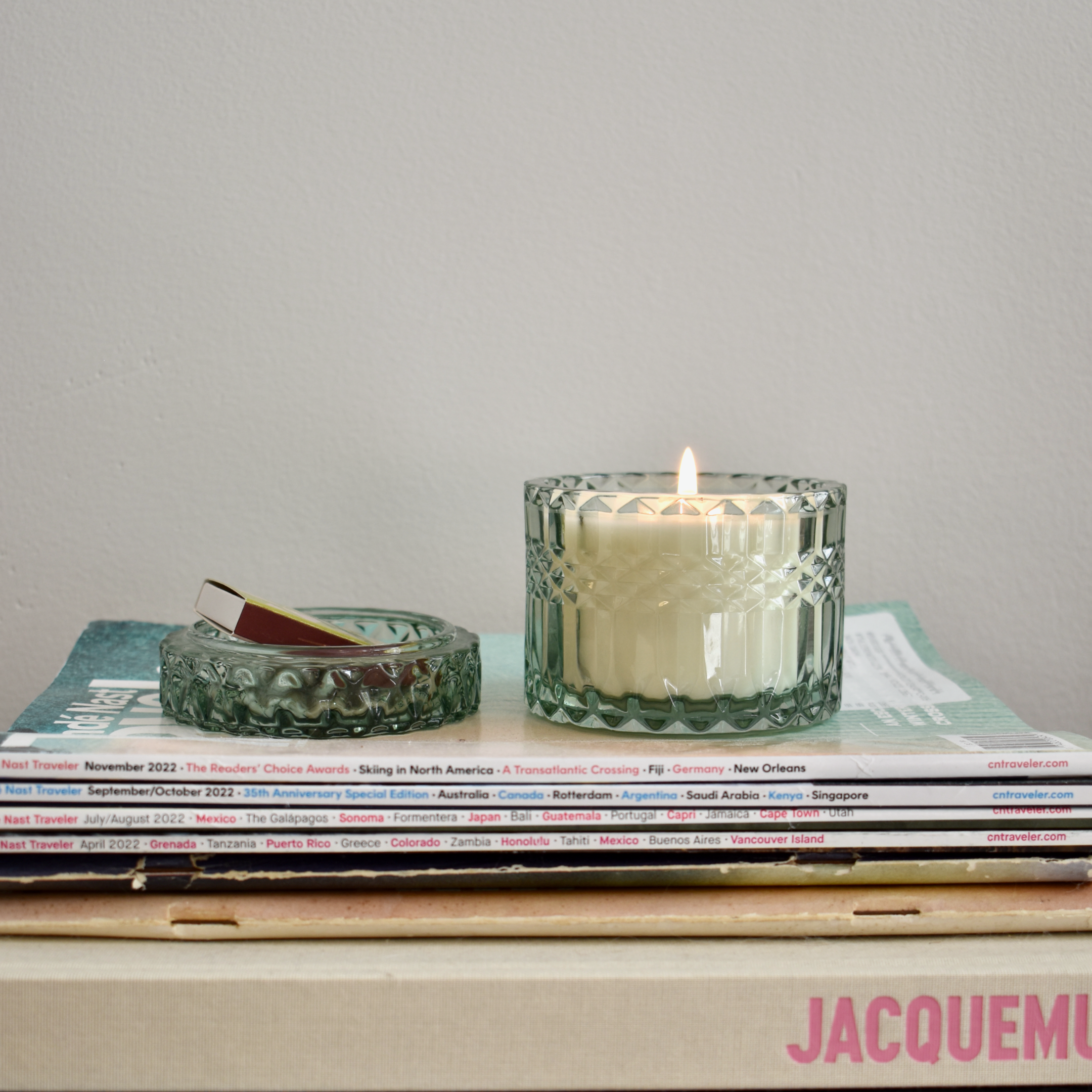 lit candle on top of coffee book stack. living room decor. mint colored antique-style vessel. holiday winter fragrance.